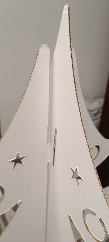 Na zdjęciu widać stojącą choinkę z bielonej, powlekanej tektury falistej. Ma prostą, nowoczesną formę z dwóch wsuwanych elementów i prezentuje się lekko oraz ekologicznie na neutralnym tle.